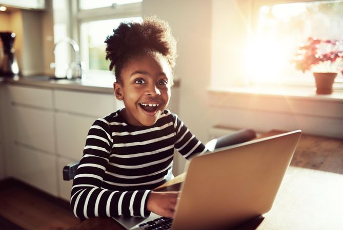 Smiling Black girl works on laptop in sunny kitchen
