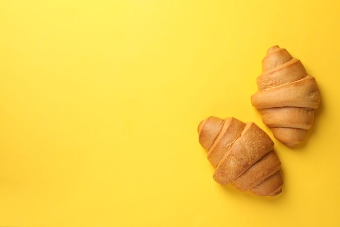 Top view of two baked croissants on yellow background, copy space