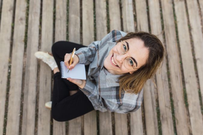 Dreamy woman sitting on boardwalk and writing in notebook in nature
