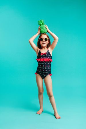 Stylish child in swimwear holding a green colored pineapple on her head