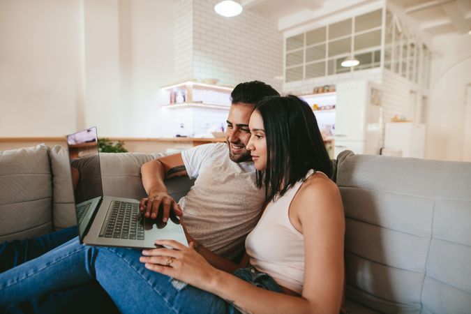 Young couple relaxing on couch with laptop at home in living room