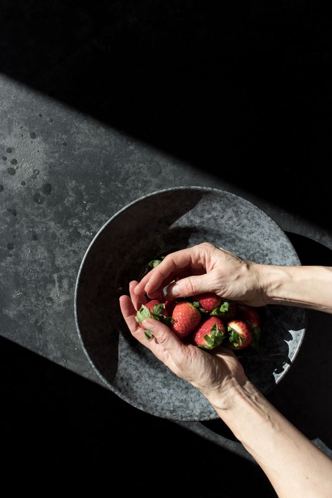 Hands with heap of strawberry near plate