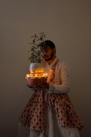 Indian man in kathak dress holding Tulsi Vivah plant surrounded with candles