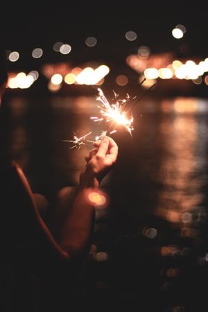 Person holding lighted sparkler at night