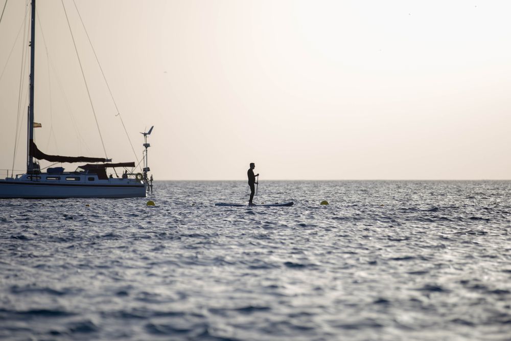 Silhouette of man kayaking beside boat during sunset