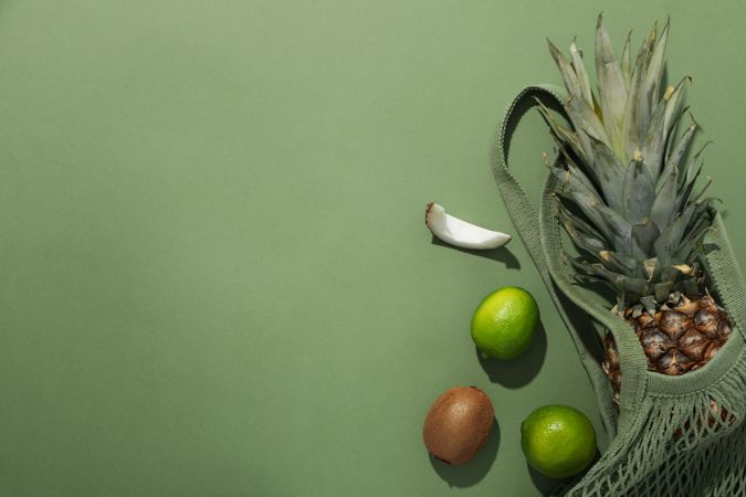 Tropical fruit in bag on green background, space for text