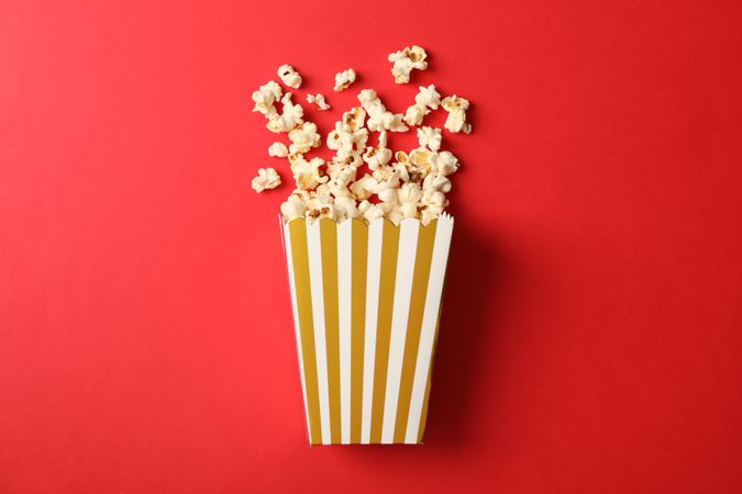 Flat lay composition with striped box and popcorn on color background