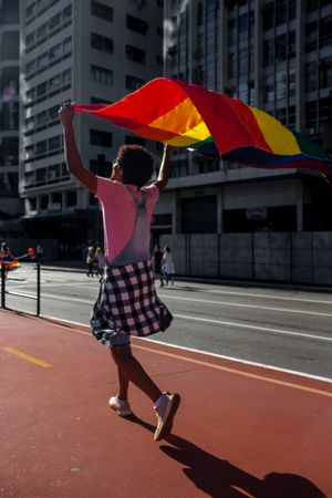 Back view of young man holding rainbow flag walking outdoor