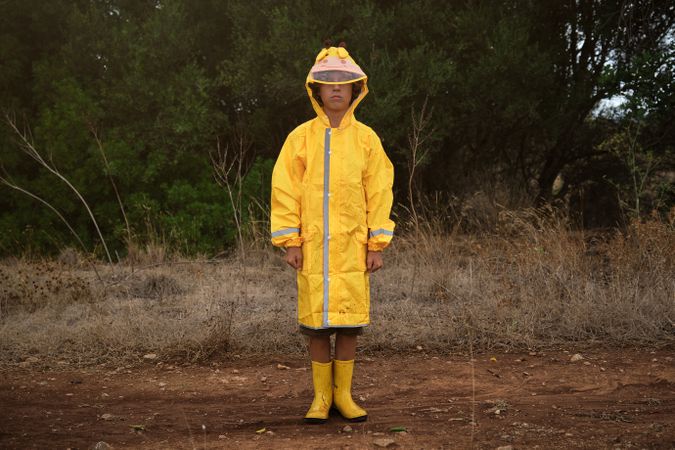 Boy in yellow raincoat and gumboots standing in forest