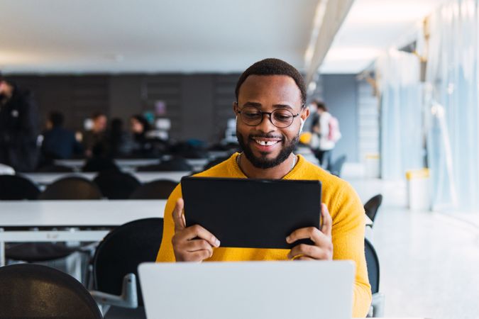 Cheerful man with earbuds using tablet and laptop at table