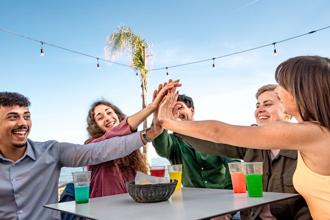 Diverse group of friends high-fiving at outdoor cafe by the sea