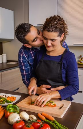Man kisses wife as she chops vegetables in kitchen