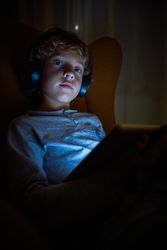 Vertical picture of a child sitting looking at a tablet with helmets at night with a distracted look