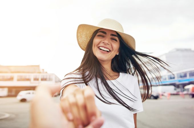 Happy woman in straw hat reaching towards camera outside