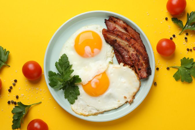 Looking down at plate of breakfast with eggs, sunny side up with bacon