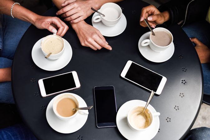 Shot of table of cappuccinos & lattes with hands and smartphones