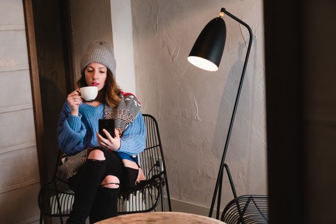 Woman in sweater and hat on the mobile phone and sitting near wall