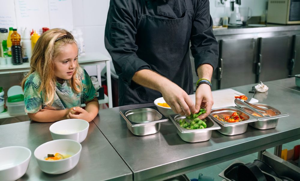 Chef preparing food with a happy young girl watching him in a professional kitchen