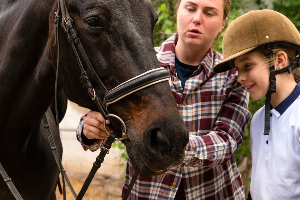 Woman teaching young rider to adjust horse's bridle.