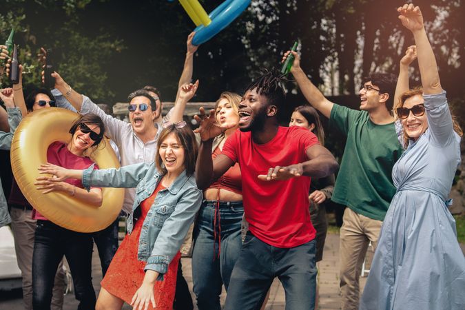 Happy excited friends on vacation dancing and drinking beers together at spring time party having fun together