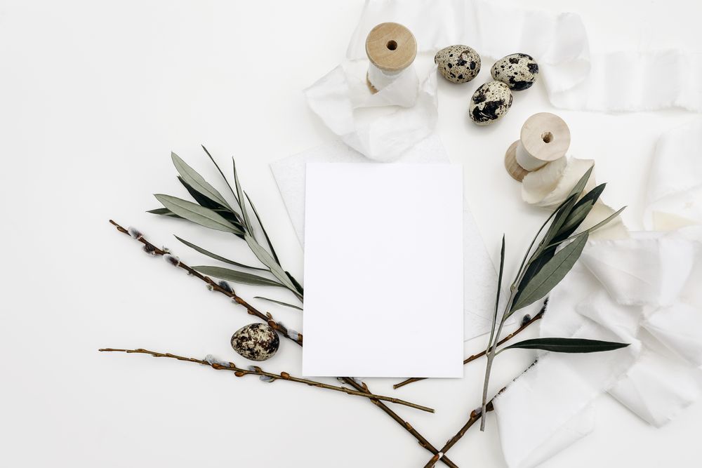 Blank greeting card, invitation mockup surrounded by quail eggs, silk ribbons, green olive tree branches and catkins