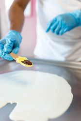 A worker is preparing a rolled ice cream with milk and chocolate chips on the freeze machine