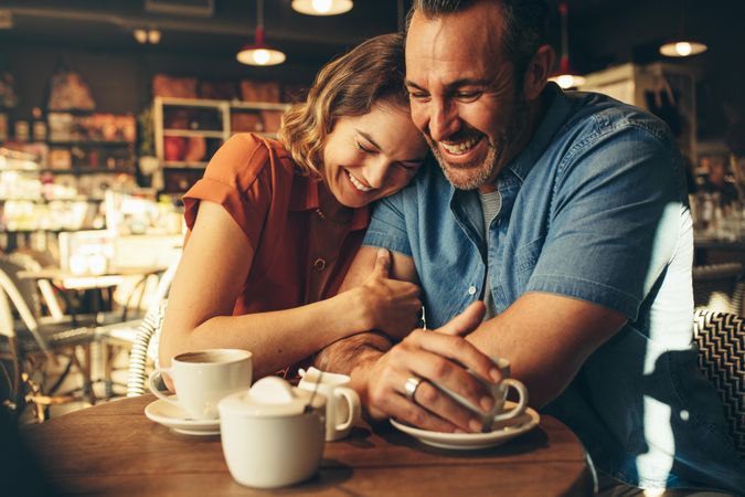 Woman smiling and putting her head on shoulder of man while sitting at a  coffee shop