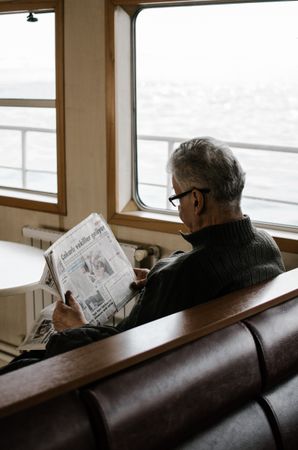 Back view of older man in brown sweater reading newspaper