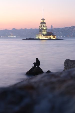 Silhouette of man sitting on rock on seashore near Maiden's tower in Istanbul, Turkey