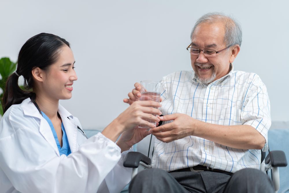 Mature man smiling while taking glass of water from medical professional