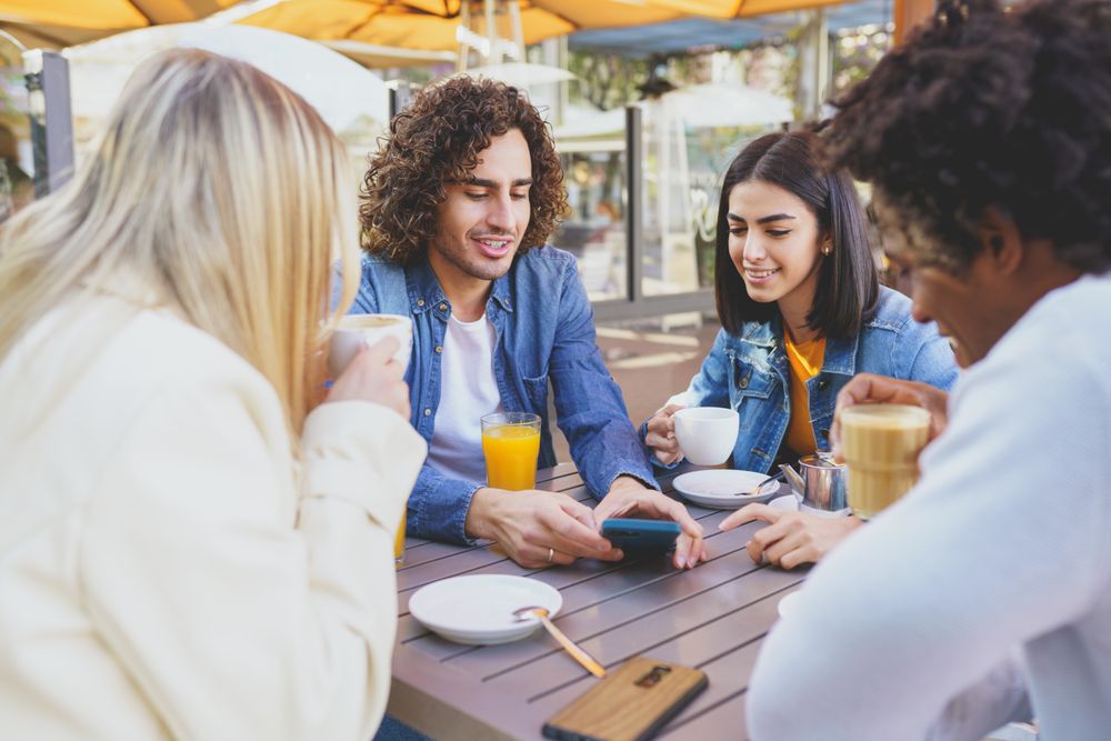 Friends looking at phone of male over coffee and juice outside