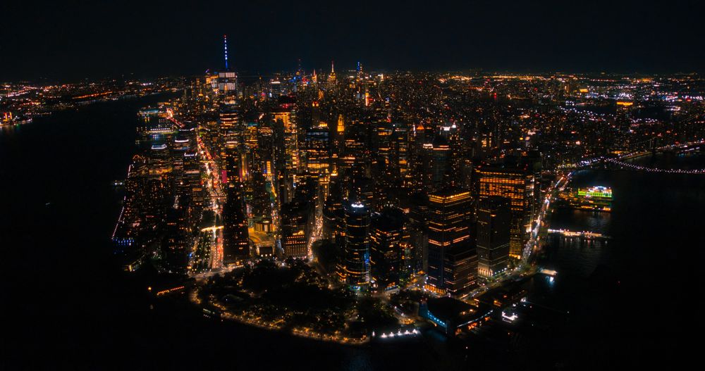 Aerial Night View of New York City Avenues in Manhattan, Business and Residential Building Roofs, Cars and Commercial Vehicles Driving at Night. Helicopter View a Straight Roads with Traffic