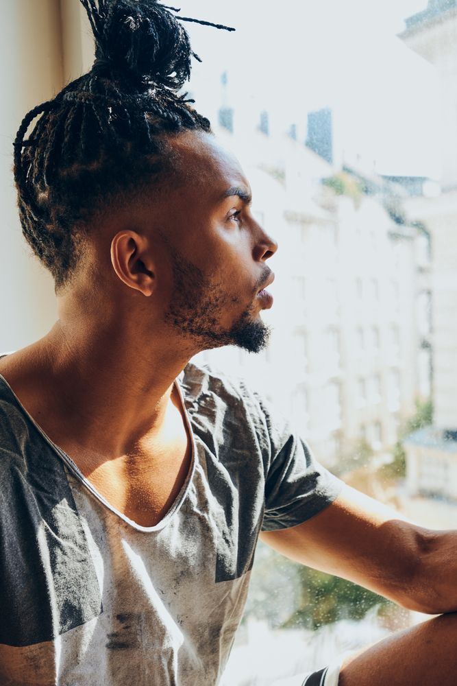 Thoughtful Black male sitting on windowsill