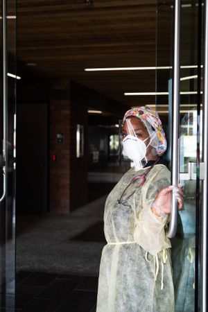 Smiling nurse in PPE holds glass door open while looking at camera