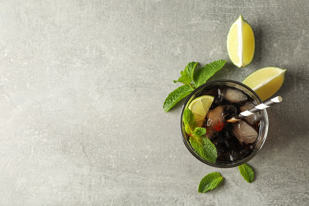 Glass with cold cola and citrus on grey table, top view