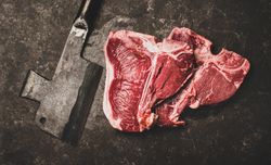 Two T-bone steaks with cleaver on butchers block, wide composition