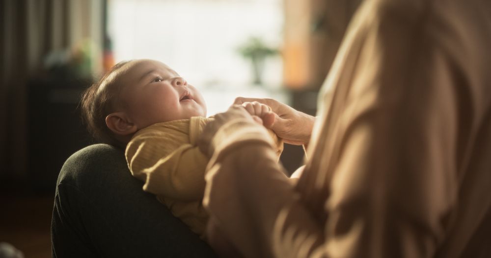 Portrait of a Cute Asian Baby Resting on her Mother's Lap, as She Holds Her Hands.