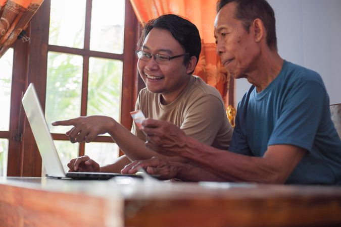 Happy adult son and mature father pay online using laptop and credit card