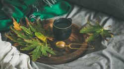 Fall leaves next to tea cup and infuser on wooden tray
