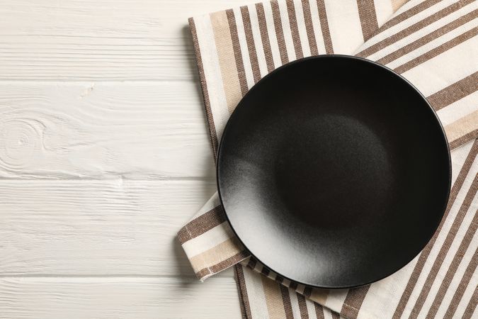 Kitchen towel with plate on wooden background, top view