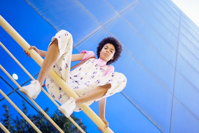 Low angle shot of woman sitting on handrails in front of  reflective glass building