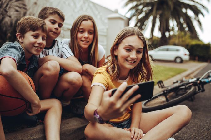 Cheerful kids taking a selfie sitting on the edge of a street