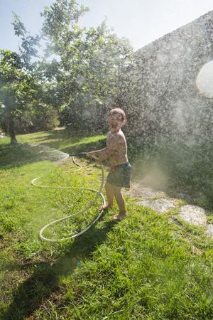 Little child having fun with garden hose and water