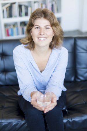 Front view portrait of a happy female with glass of water sitting on couch in cosy home