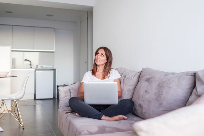 Smiling woman sitting on sofa working on her laptop in the morning