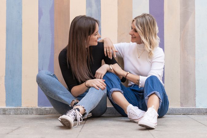 Happy girlfriends sitting against painted urban wall