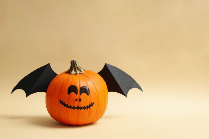 Pumpkins with smile and wings on beige background