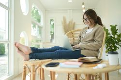 A young woman sits with her legs stretched using a laptop in a comfortable posture.