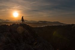 Traveler on high coastal cliff in sunset