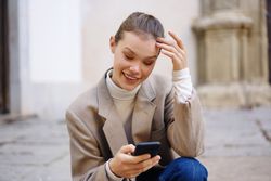 A young woman happily enjoying the use of her mobile phone while outdoors among nature